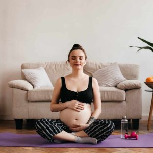 Cheerful brunette pregnant woman enjoys music in white wireless headphones and gently touches belly